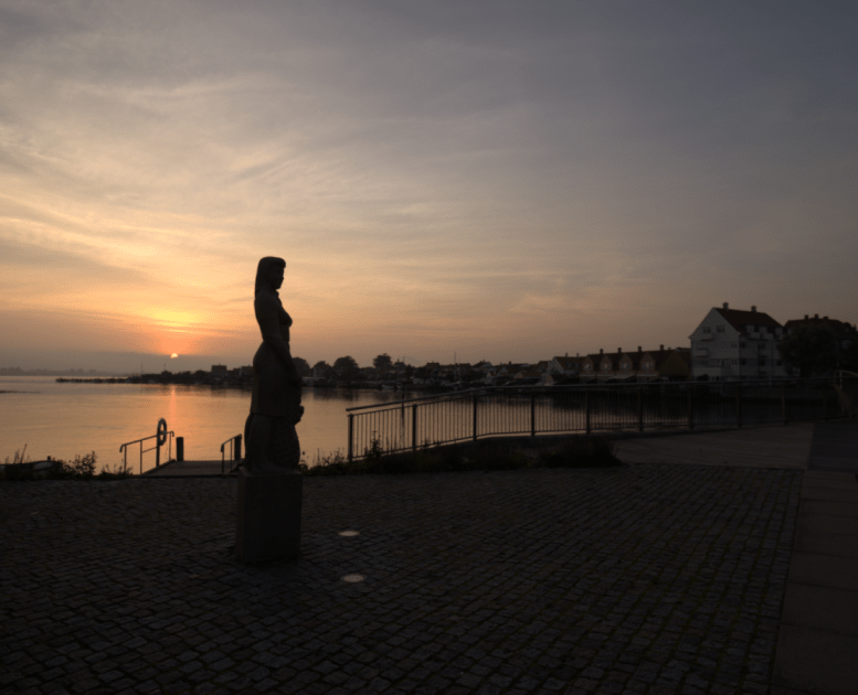 Statuen Amanda ved Langebro i Kerteminde. I baggrunden solnedgang over Lillestranden